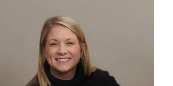 Smiling woman with blonde hair wearing a black top against a plain background.