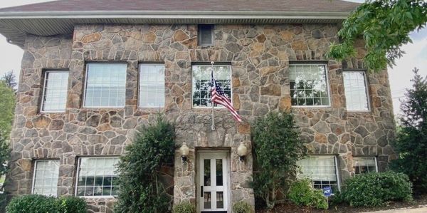 Two-story stone house with symmetrical windows and an American flag.