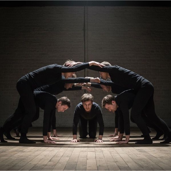 A group of seven people in black forming a symmetrical arch with their bodies.