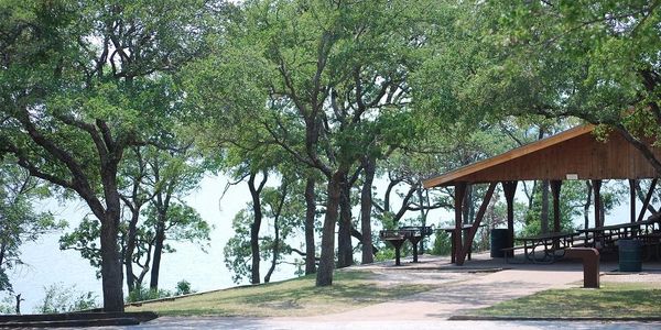 A peaceful lakeside picnic shelter surrounded by trees and greenery.