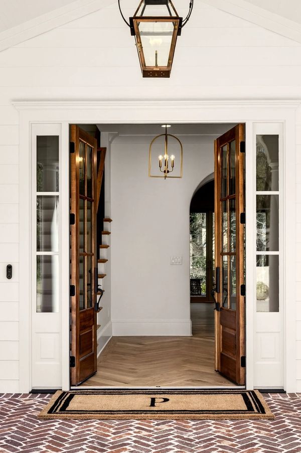Open wooden doors reveal a bright, minimalist interior with a monogrammed doormat.