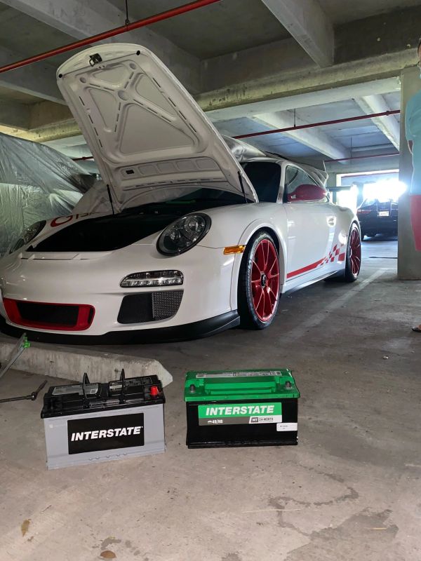 White sports car with red rims and open hood in garage.