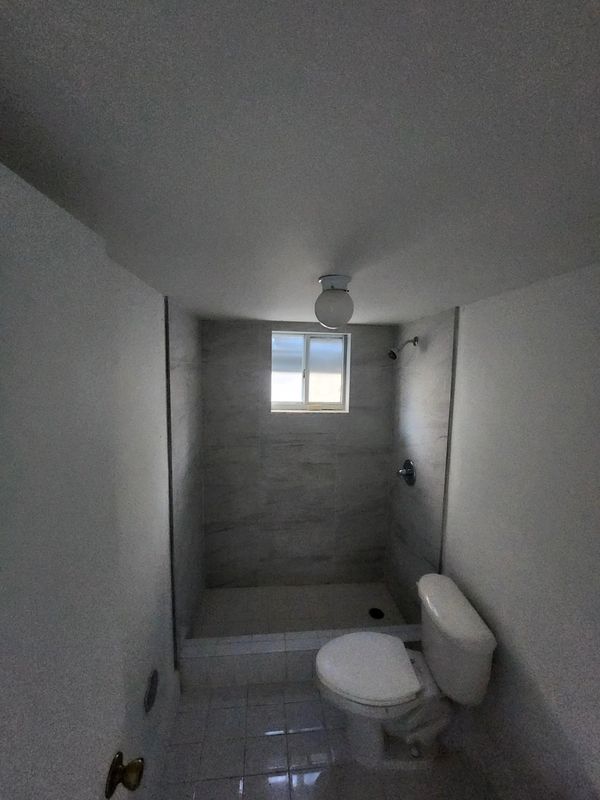 Small bathroom with toilet and shower, tiled floor and walls.