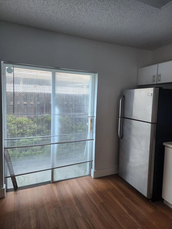Kitchen corner with a silver refrigerator and closed window blinds.
