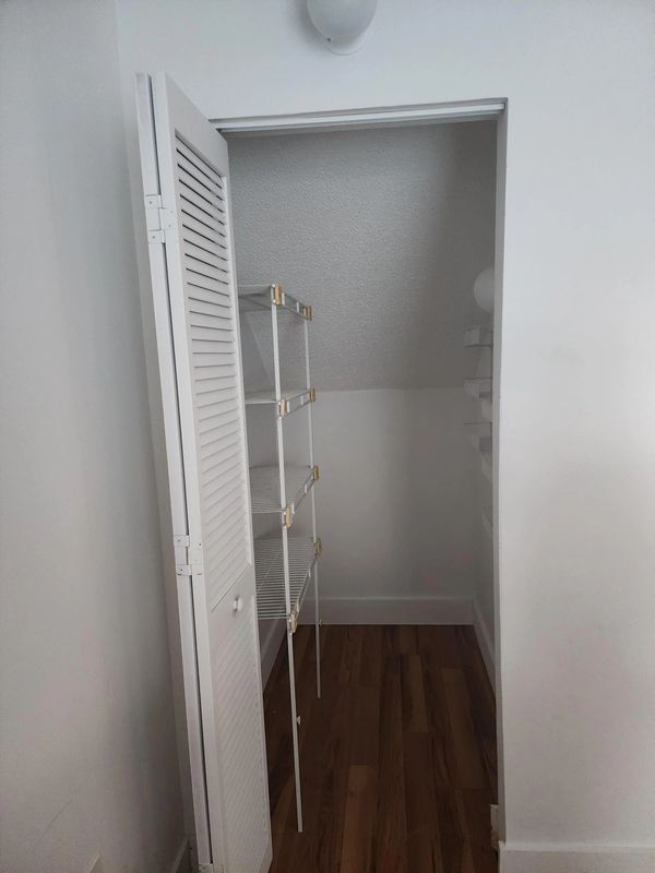 Empty small white closet with wire shelves and wooden floor.