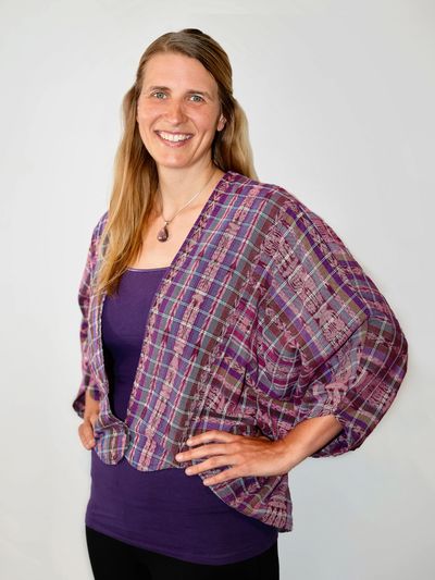 Smiling woman in a purple top and plaid jacket.