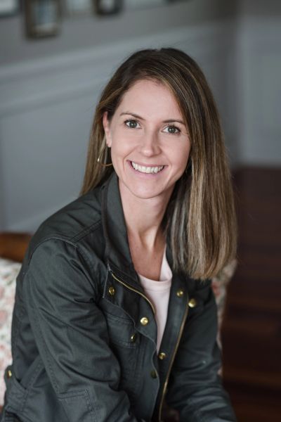 Smiling woman with straight hair wearing a dark jacket indoors.