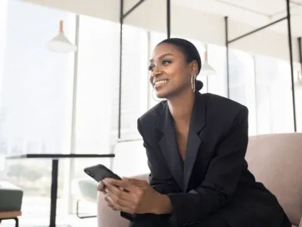 A confident woman sitting and holding a phone, smiling.