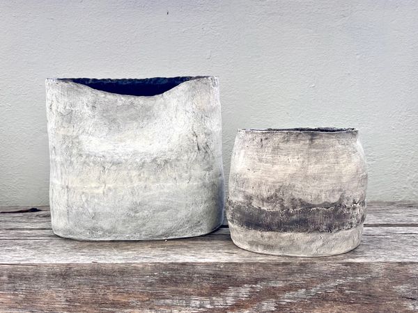 Two rustic, handmade ceramic pots on a wooden surface against a plain wall.