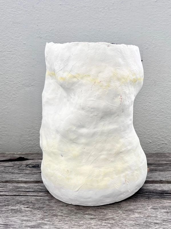 A white, textured ceramic vase on a wooden surface against a gray wall.