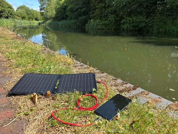 Portable solar charger and phone by a peaceful riverside.