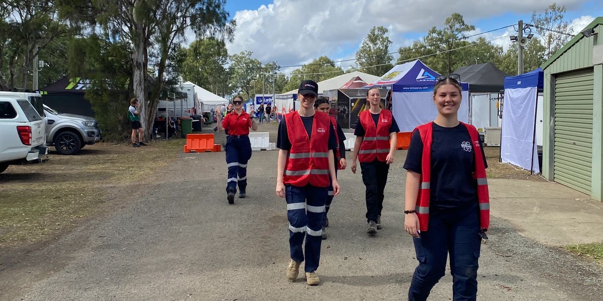 Group of medics walking outdoors at an event with tents and vehicles.