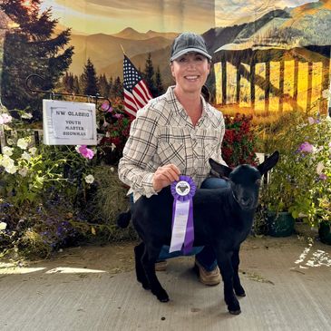 A woman proudly holds a purple ribbon with her black goat at a livestock show.