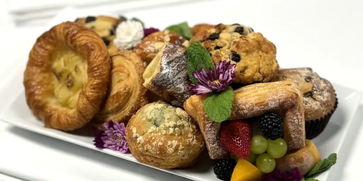 A plate of assorted pastries and muffins garnished with fresh fruit and flowers.
