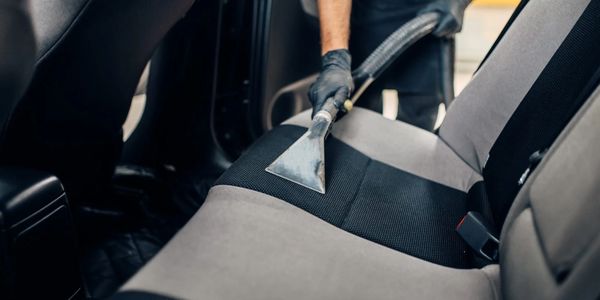 Person vacuuming the back seat of a car with a professional cleaner.