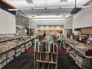 A library room with bookshelves and people browsing.