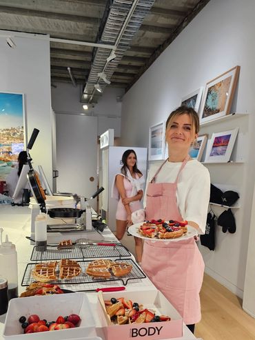 Woman in pink apron serving waffles topped with berries in a bright cafe.
