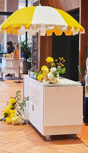 A white cart with a yellow and white umbrella decorated with yellow and white flowers indoors.