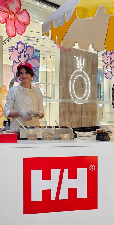 Woman serving food at a Helly Hansen branded booth with colorful decorations.