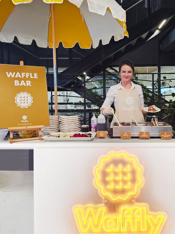Smiling woman serving waffles at a bright Waffly waffle bar stand.
