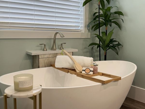Modern white freestanding bathtub with a wooden tray and bath accessories.