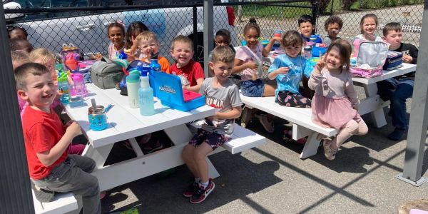 Children eating lunch outdoors at picnic tables.