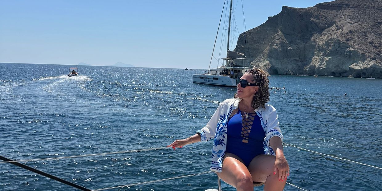 Woman in blue swimsuit relaxing on a boat with sea and cliffs in background.