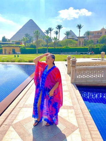 Woman in colorful dress near pool with pyramid in background.