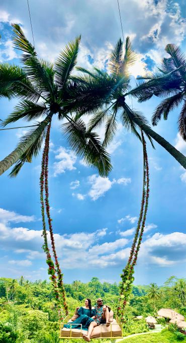 Couple enjoying a swing between two tall palm trees.