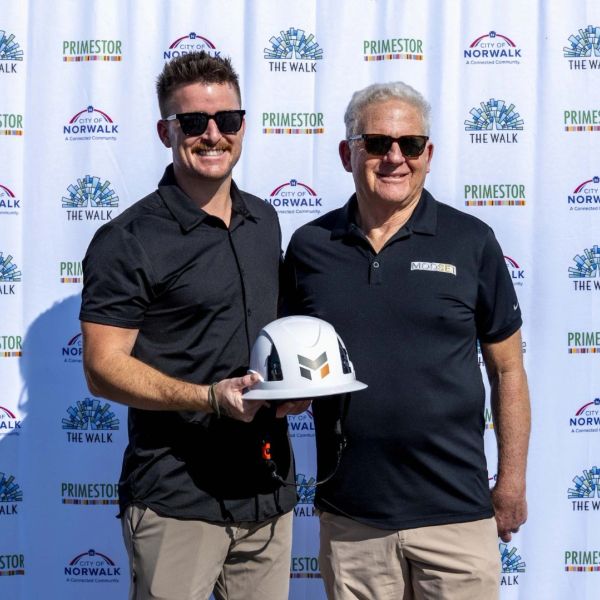 Two men in sunglasses holding a white hard hat at a city event.