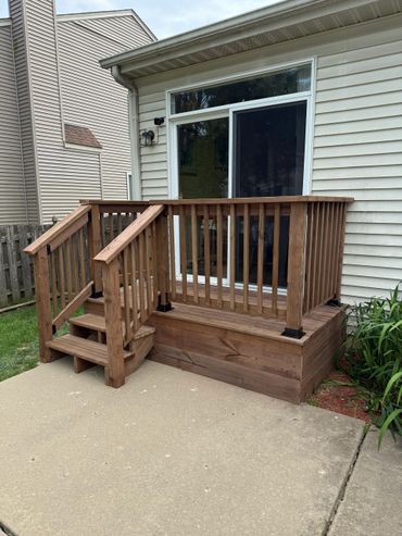 Small wooden deck with stairs leading to a sliding glass door.
