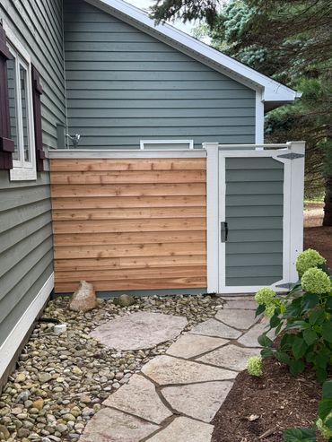 Stone pathway leading to a wooden gate beside a house with green siding.