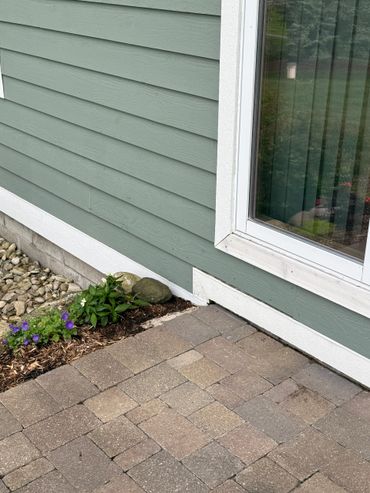 Corner of a house with a stone patio and small garden.