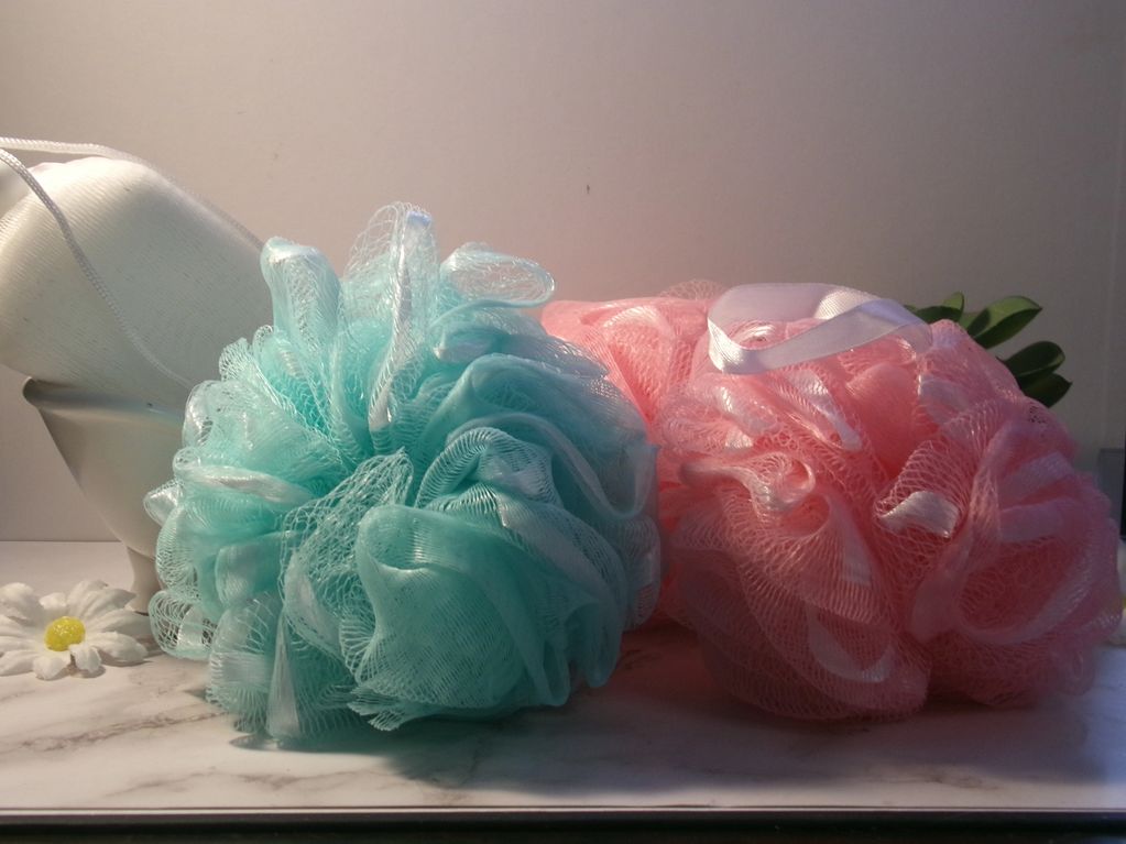Two bath poufs, one blue and one pink, sitting on a marble surface.