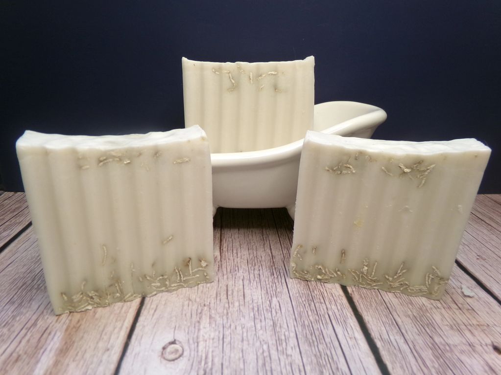 Three bars of handmade soap with natural textures displayed on a wooden surface.