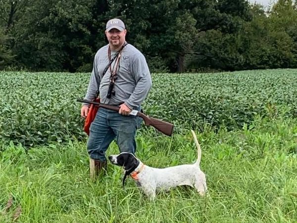 Man with hunting dog in a field holding a shotgun.
