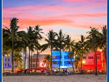 Palm trees and colorful buildings line a beach at sunset.