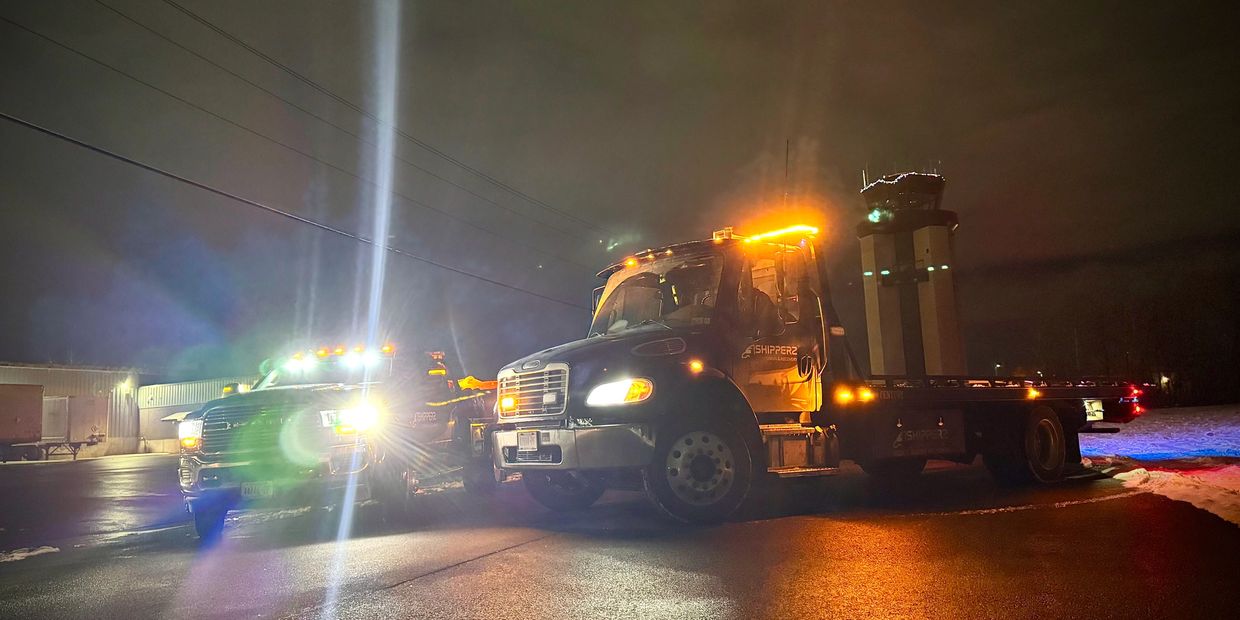 Two trucks with bright lights on a wet road at night.