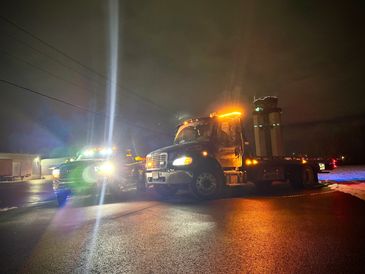 Two trucks with bright lights parked at night near a control tower.