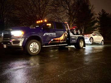 A tow truck carrying a silver car at night on a wet road.