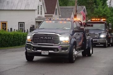A dark blue RAM tow truck with flashing lights on a residential street.