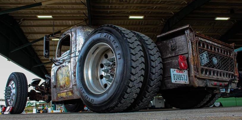 Rusty custom lowrider truck with large Falken tires under a metal roof.