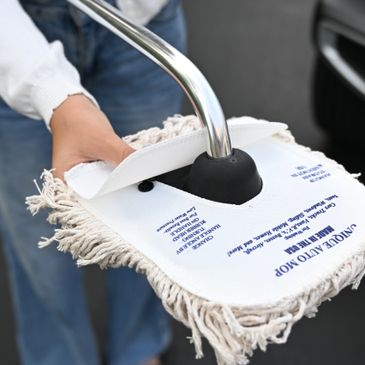 Person holding a mop with a white cloth cover and metal handle outdoors.