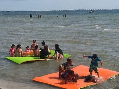 12 people in water playing on 2 large water mats in tampa bay beach. www.whatsuppaddlesports.com