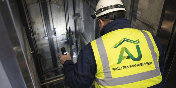 Facilities worker inspecting elevator shaft wearing high-visibility vest and helmet.