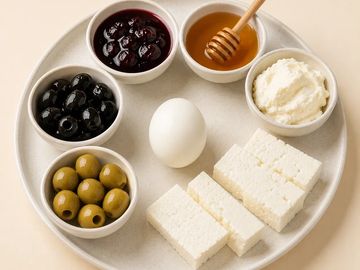 A plate with olives, cheese, honey, jam, an egg, and cream cheese.