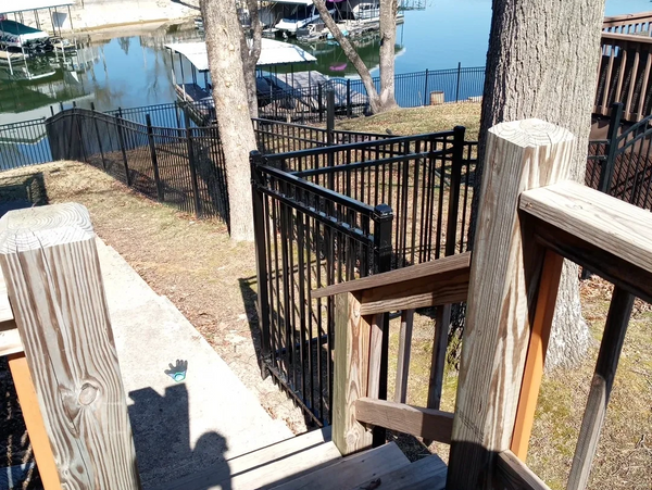 Wooden stairs leading down to a lakeside dock area with black metal fencing.