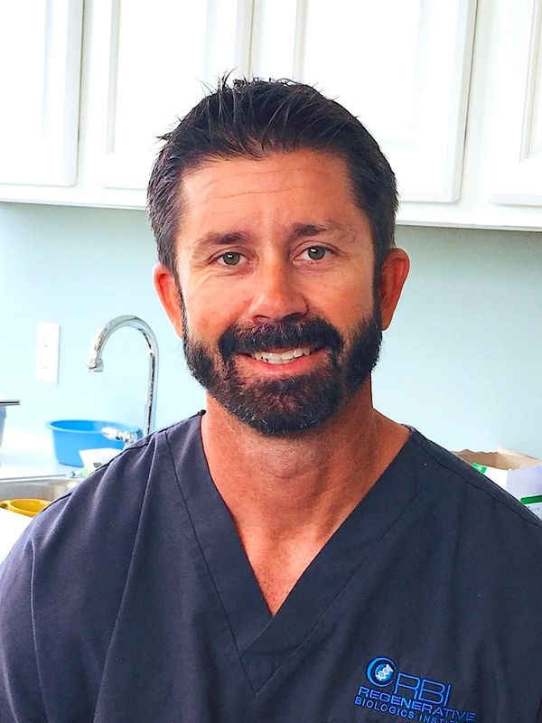 Smiling man in medical scrubs with RBI Regenerative Biology logo.