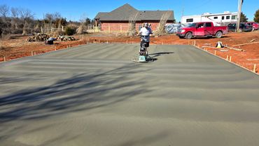 Worker smoothing freshly poured concrete slab with a power trowel.