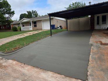 Freshly poured concrete driveway under a carport beside a suburban home.